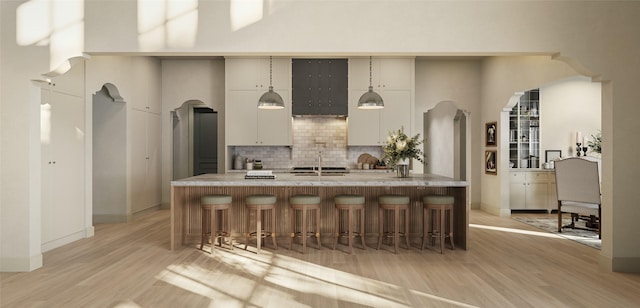 kitchen featuring light wood-style floors, arched walkways, backsplash, and a breakfast bar