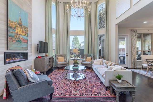 living room featuring a tiled fireplace, a notable chandelier, wood finished floors, and a towering ceiling