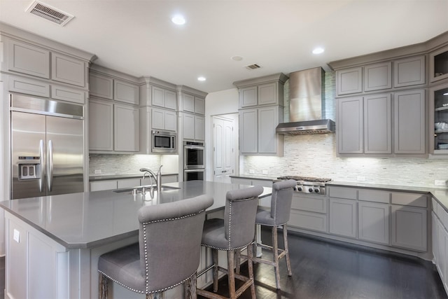 kitchen with visible vents, gray cabinetry, a sink, wall chimney range hood, and built in appliances