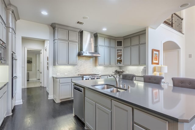 kitchen with visible vents, gray cabinetry, a sink, stainless steel dishwasher, and wall chimney exhaust hood