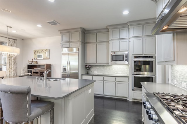 kitchen featuring under cabinet range hood, built in appliances, decorative backsplash, and a sink