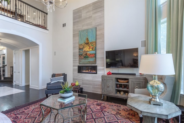 living area featuring arched walkways, visible vents, a tiled fireplace, and wood finished floors