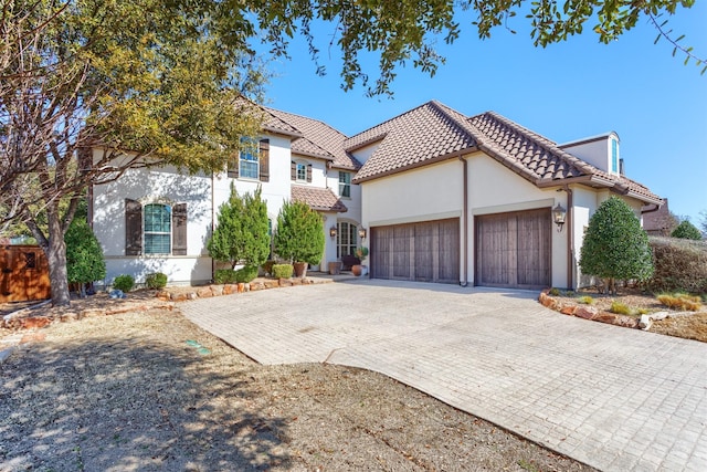 mediterranean / spanish-style house with stucco siding, a tile roof, decorative driveway, and a garage