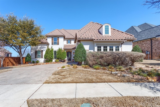 view of front of property featuring stucco siding, driveway, a tile roof, and fence