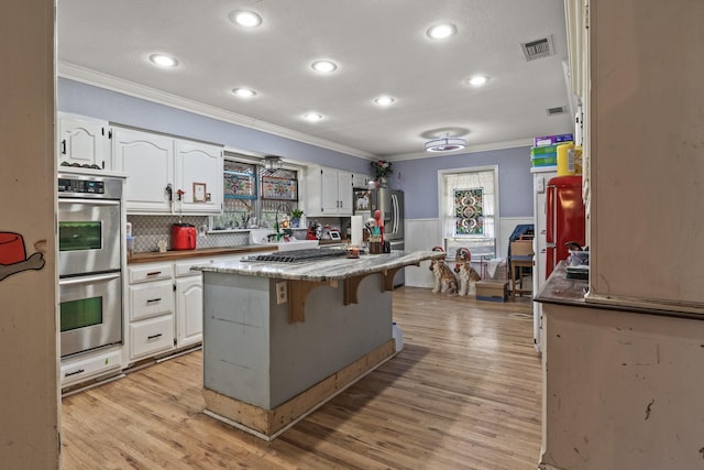 kitchen featuring a center island, ornamental molding, wainscoting, appliances with stainless steel finishes, and white cabinets