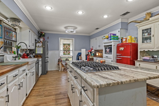 kitchen featuring a sink, stainless steel appliances, wainscoting, crown molding, and light wood-type flooring