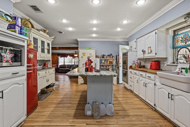 kitchen featuring ornamental molding, a kitchen bar, visible vents, and white cabinets