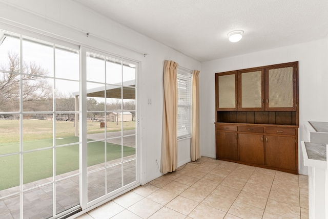 doorway to outside with light tile patterned floors, a wealth of natural light, and a textured ceiling