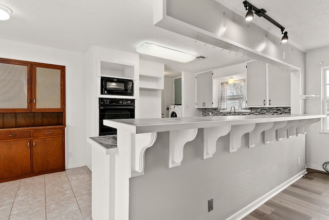 kitchen with a kitchen bar, black appliances, a textured ceiling, a peninsula, and washer / dryer