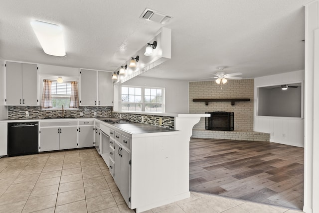 kitchen featuring visible vents, a brick fireplace, open floor plan, dishwasher, and a peninsula