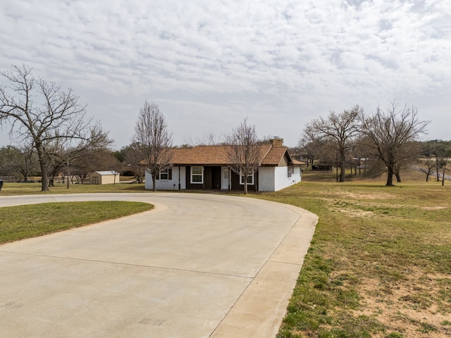 view of front of house featuring curved driveway, a chimney, and a front yard