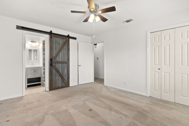 unfurnished bedroom with visible vents, ensuite bathroom, a barn door, a closet, and carpet