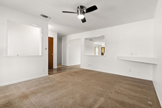 carpeted empty room with visible vents, a textured ceiling, baseboards, and ceiling fan