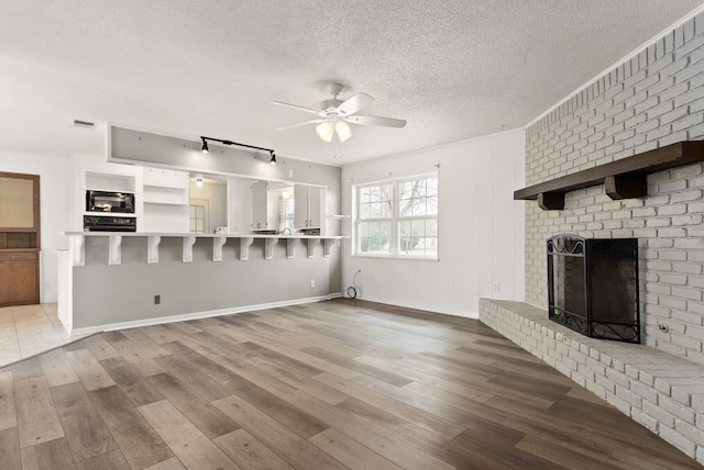 unfurnished living room with a textured ceiling, wood finished floors, a fireplace, baseboards, and ceiling fan