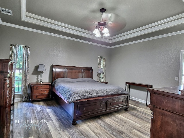 bedroom featuring ceiling fan, visible vents, wood finished floors, and crown molding