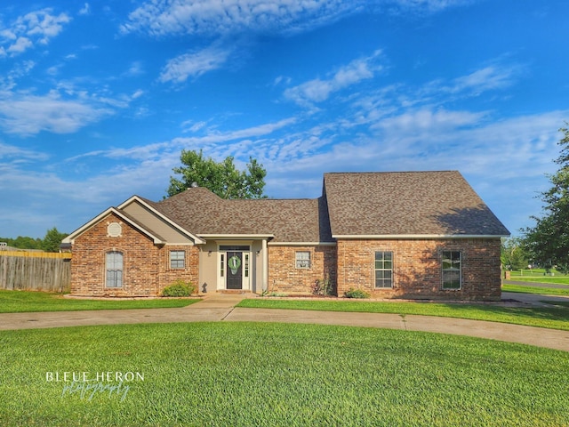 view of front of home with brick siding, roof with shingles, a front lawn, and fence