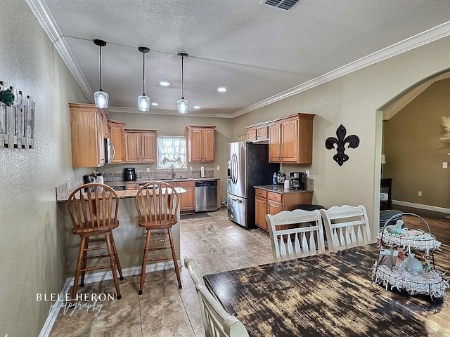 kitchen featuring a sink, stainless steel appliances, arched walkways, a peninsula, and baseboards