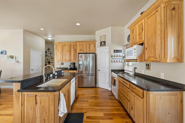 kitchen featuring dark countertops, white appliances, a kitchen island with sink, and a sink