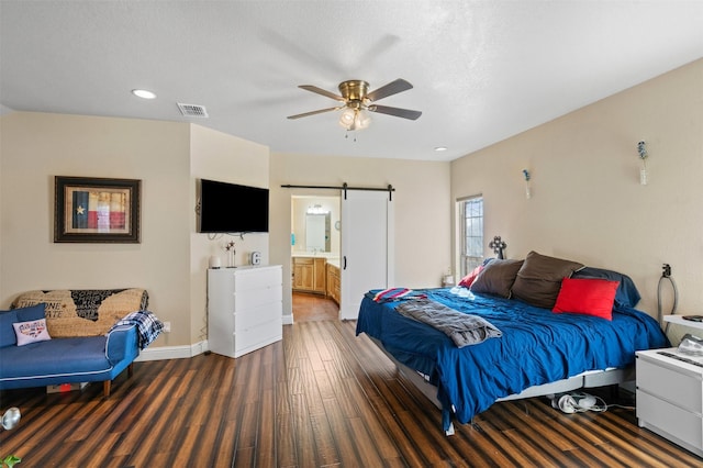 bedroom with visible vents, ceiling fan, baseboards, a barn door, and wood finished floors