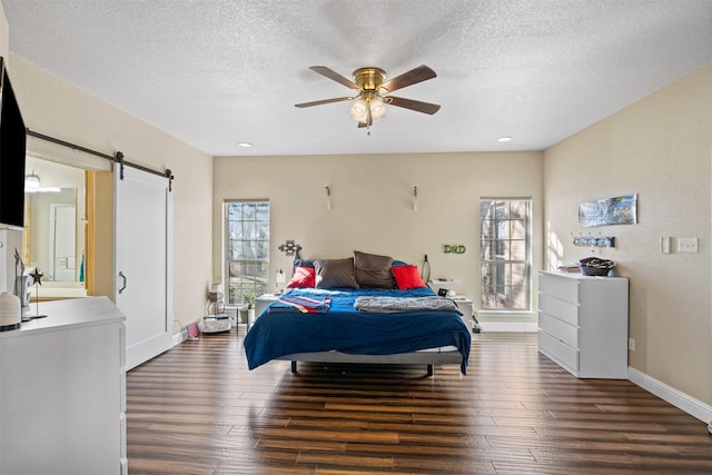 bedroom featuring a barn door, wood finished floors, baseboards, and a textured ceiling