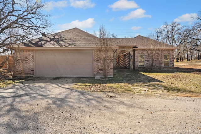 ranch-style home featuring gravel driveway, a garage, brick siding, and roof with shingles