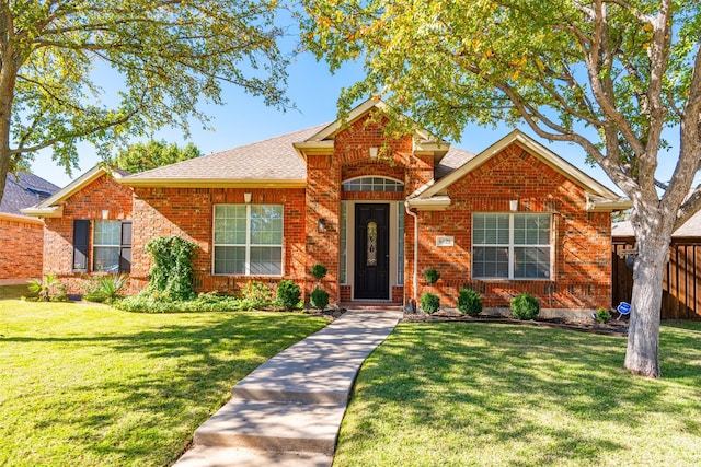 view of front of house featuring brick siding, roof with shingles, a front lawn, and fence