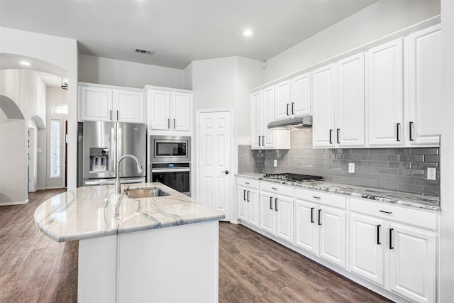 kitchen with under cabinet range hood, decorative backsplash, arched walkways, stainless steel appliances, and a sink