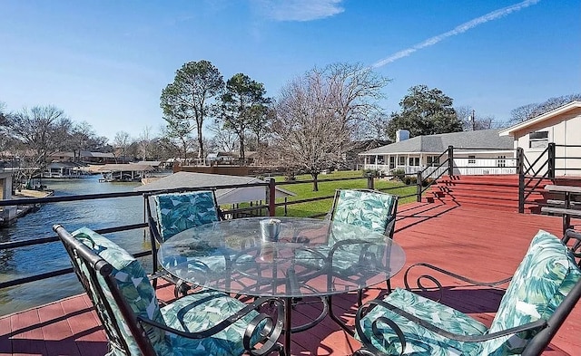 wooden deck featuring outdoor dining area, a lawn, and a water view