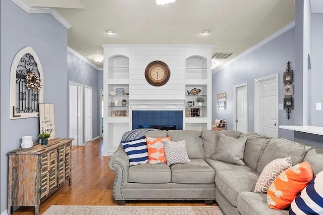 living room with visible vents, crown molding, built in features, a fireplace, and wood finished floors