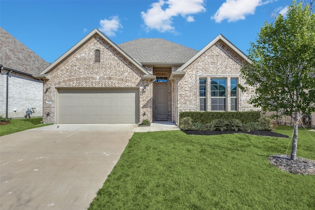 french country home with a front yard, roof with shingles, an attached garage, concrete driveway, and brick siding