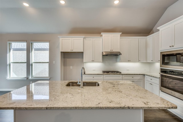 kitchen with a sink, stainless steel appliances, vaulted ceiling, under cabinet range hood, and white cabinetry