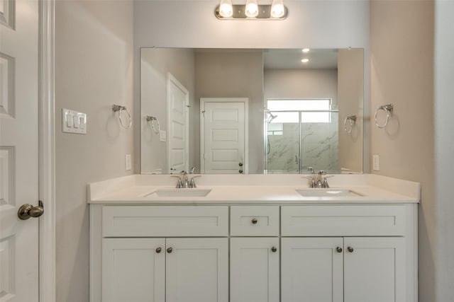 full bath with a sink, a marble finish shower, and double vanity