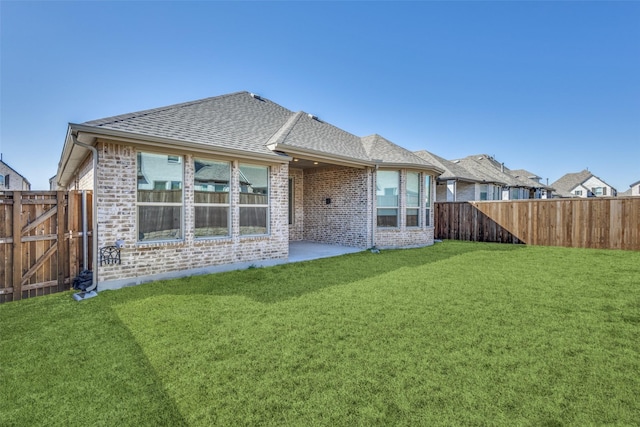 rear view of house with roof with shingles, a yard, a fenced backyard, a patio area, and brick siding