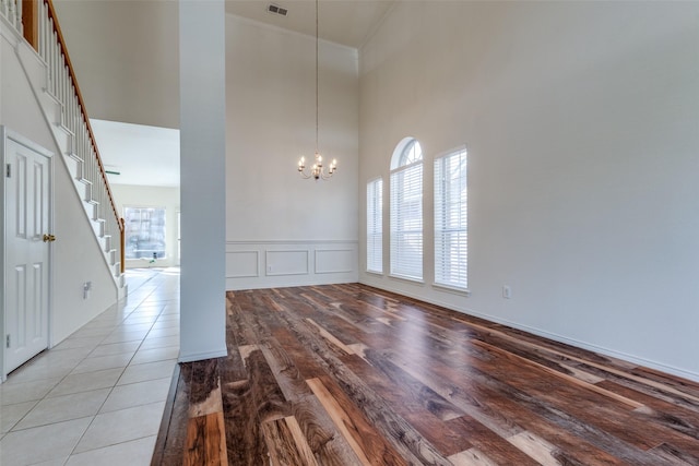 spare room featuring stairway, light wood finished floors, crown molding, a decorative wall, and a chandelier