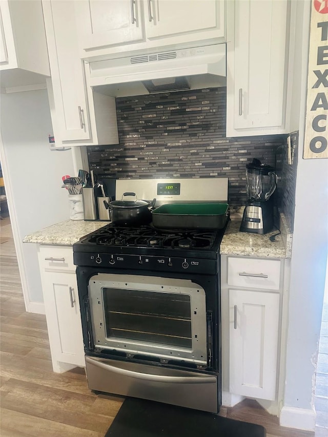 kitchen featuring under cabinet range hood, stainless steel range with gas stovetop, white cabinetry, and tasteful backsplash