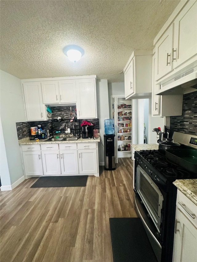 kitchen with under cabinet range hood, gas range, white cabinetry, and wood finished floors