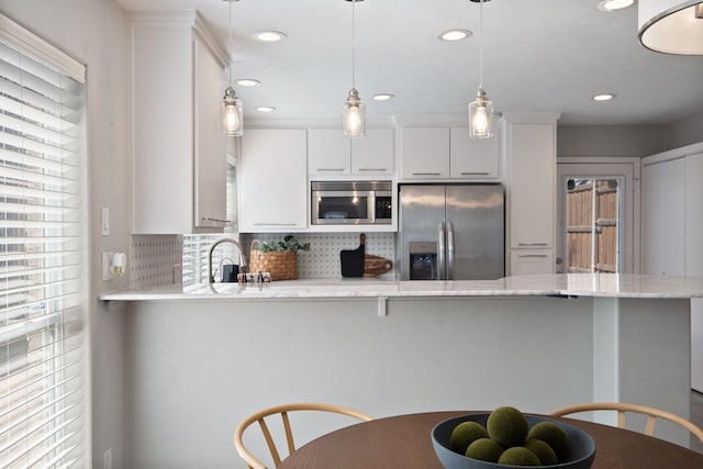 kitchen with a sink, hanging light fixtures, stainless steel appliances, white cabinetry, and backsplash