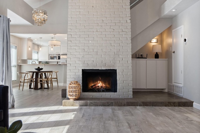 living area featuring visible vents, a brick fireplace, baseboards, and wood finished floors