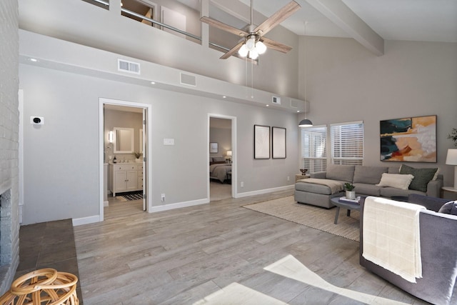 living area with visible vents, beamed ceiling, a fireplace, and light wood finished floors