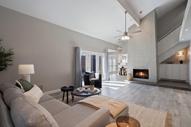 living room with beam ceiling, high vaulted ceiling, wood finished floors, a fireplace, and ceiling fan