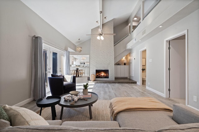 living room with light wood-style floors, a fireplace, visible vents, and high vaulted ceiling