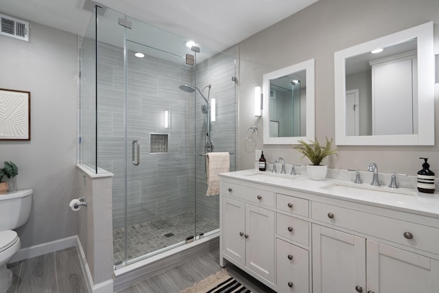 full bath with visible vents, double vanity, a sink, a shower stall, and toilet