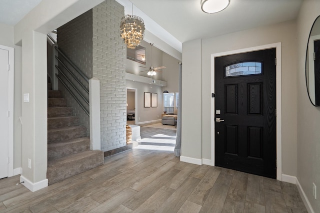 foyer featuring wood finished floors, baseboards, a high ceiling, stairs, and ceiling fan with notable chandelier