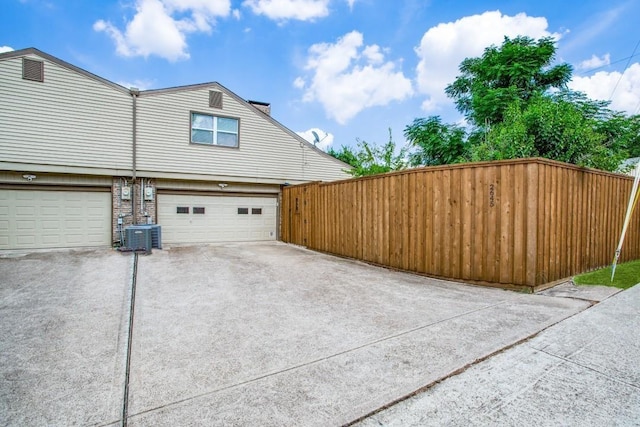 view of home's exterior with central AC unit, an attached garage, driveway, and fence