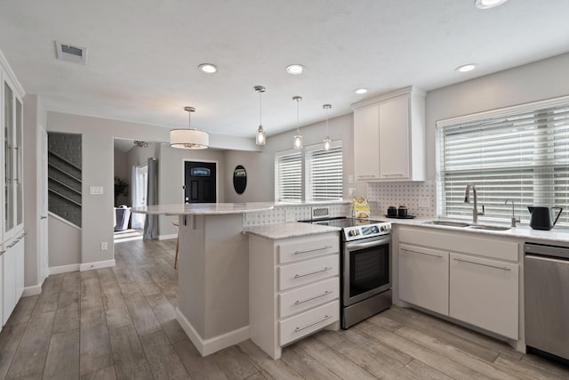 kitchen with visible vents, a sink, stainless steel appliances, a peninsula, and light wood finished floors