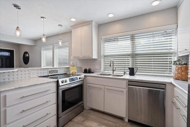 kitchen with decorative backsplash, appliances with stainless steel finishes, hanging light fixtures, white cabinets, and a sink