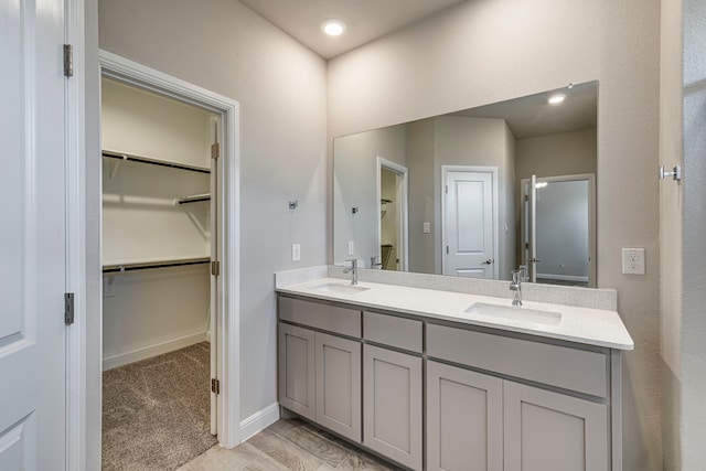 full bath with double vanity, a spacious closet, baseboards, and a sink