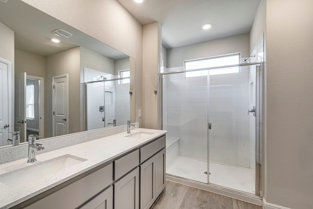 full bathroom featuring a shower stall, wood finished floors, double vanity, and a sink