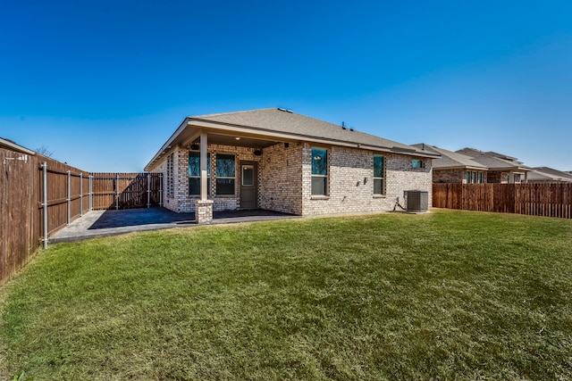 rear view of property with central air condition unit, a lawn, a fenced backyard, brick siding, and a patio area