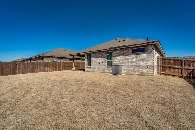 rear view of property featuring a fenced backyard, a lawn, brick siding, and central AC